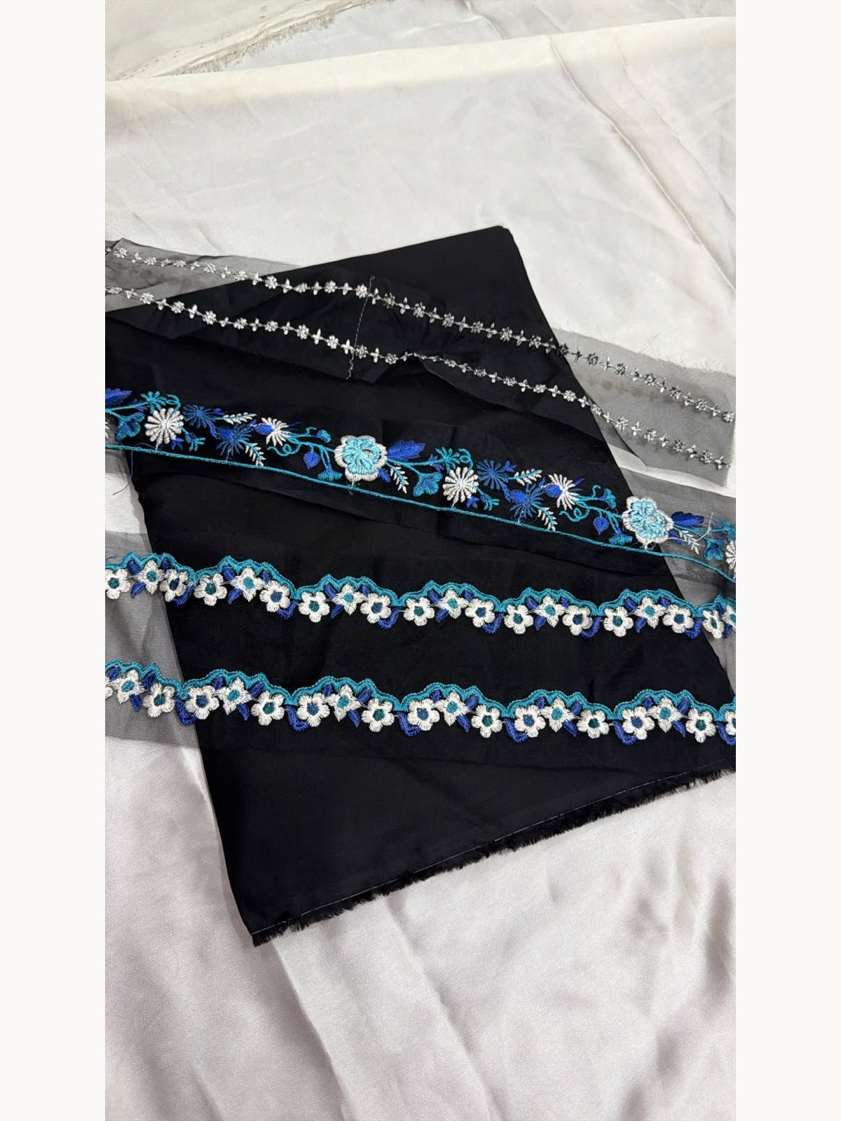 Black viscose fabric with blue and white floral embroidery and decorative borders – close-up